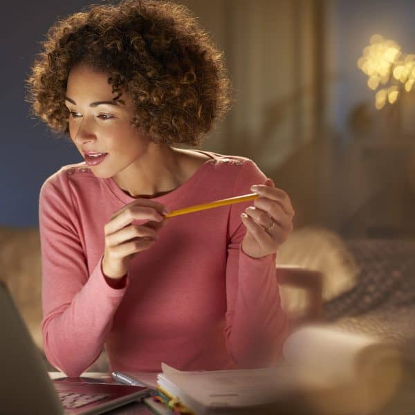 a young woman works at home at night , going through her paperwork and bills .she is working at her laptop . She could be running her own business or returning to part time education .